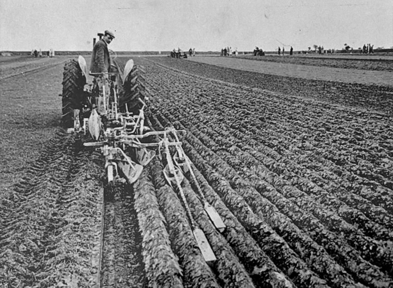 old fashioned plough and tractor ploughing a field