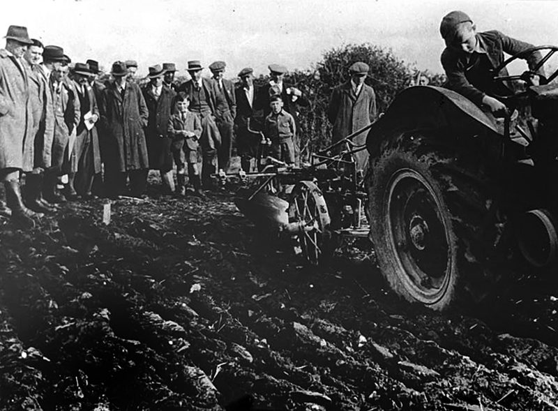 black and white image of old tractor and plough